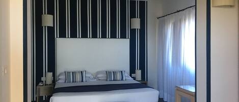 A modern hotel room with a large bed, striped wall panels, and a bedside table with a lamp.