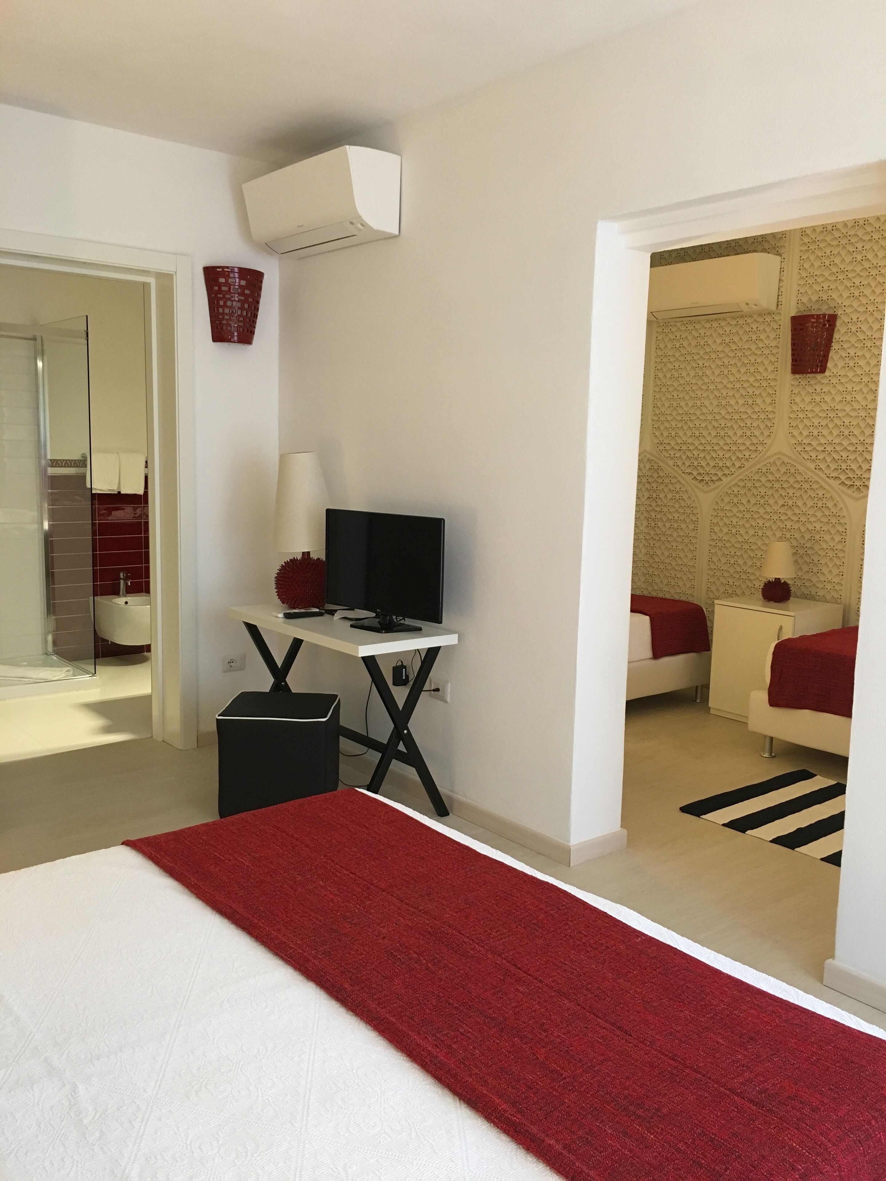 Een moderne hotelkamer met een bed, een bureau met een computer, een kleine prullenbak en een badkamer die door een geopende deur zichtbaar is.