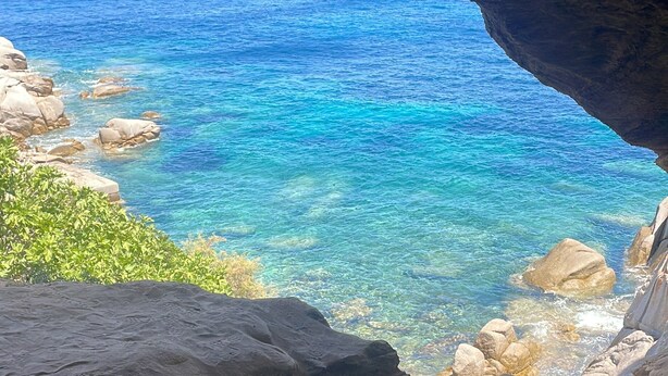 A natural cave opening with clear blue water and rocky terrain.