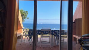 A room with a view of the ocean, a table with chairs, and a window with curtains.