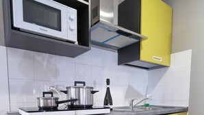 Een kleine keuken met een magnetron, kookplaat en spoelbak. Het heeft gele kastjes en een witte koelkast.