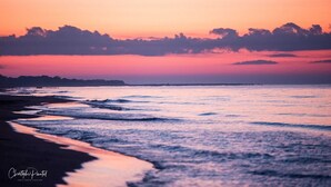 Una playa al atardecer con olas, cielo despejado y una costa distante.