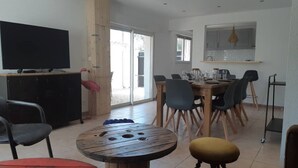 Amplia sala de estar con una mesa de comedor, sillas, televisor y una zona de cocina con armarios y una lámpara colgante.