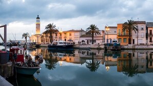 Un pueblo costero con edificios históricos, un faro y barcos amarrados en aguas tranquilas.
