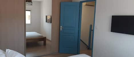 A bedroom with a bed, a wardrobe, a mirror, and a television on the wall.