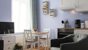 A modern kitchen with white cabinets, a dining area with a table and chairs, and a grey armchair. - Nice apartment lilac central (Bremen)