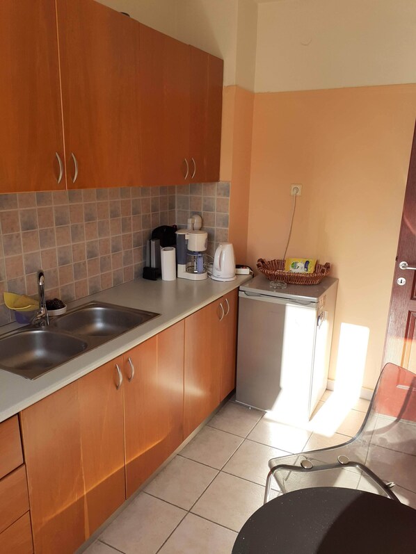 A kitchen with wooden cabinets, a stainless steel sink, a coffee maker, and a small refrigerator.