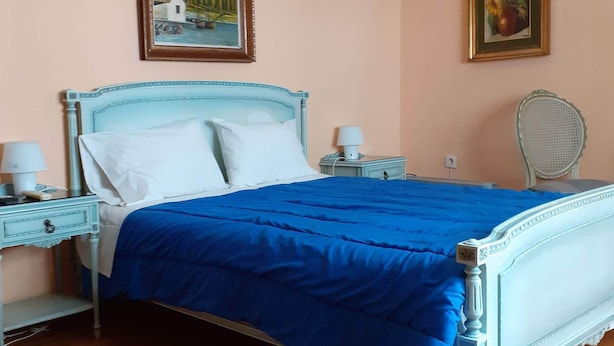 A bedroom with a bed, a nightstand, a chair, and two framed pictures on the wall. - Elegant Apartment (Athens)