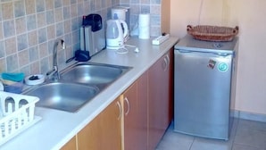 A compact kitchen with wooden cabinets, a stainless steel sink, a small refrigerator, and a tiled backsplash. - Elegant Apartment (Athens)