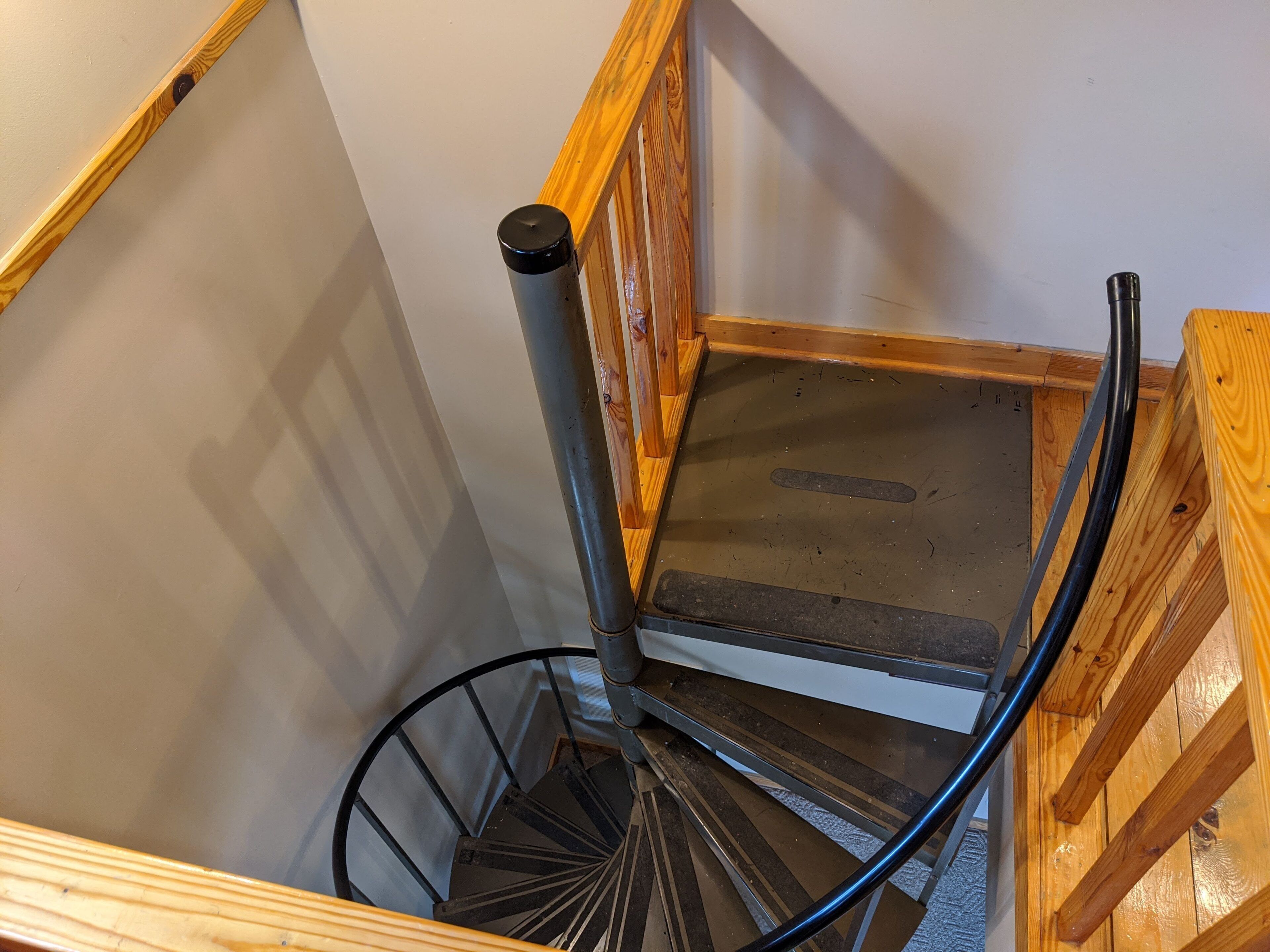Una escalera de madera con barandilla de metal y un tubo negro que recorre la estructura verticalmente.