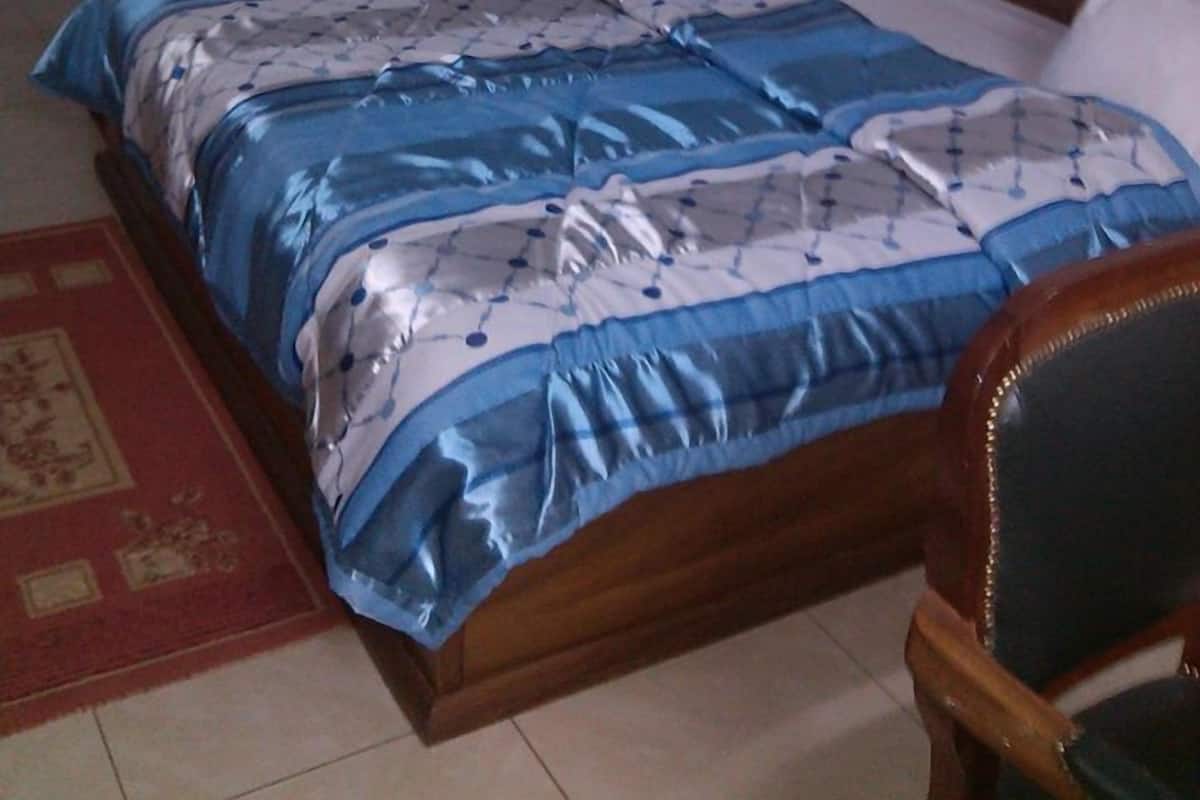 A bedroom with a large bed, a wooden nightstand with a lamp, a mirror, and a small table.