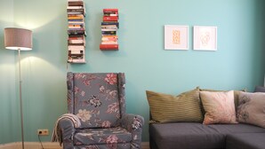 A living room with a floral armchair, a grey sofa, and a bookshelf against a teal wall. - Nice apartment turquoise central (Bremen)