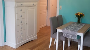 A dining area with a white cabinet, grey chairs, and a table with a floral tablecloth. - Nice apartment turquoise central (Bremen)
