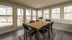 A dining area with a wooden table and chairs, large windows, and a view of a lake. - Newly Constructed 3 Bedroom, 2 Bath Home on 12.5 Acres, Water Access and Views (WestBrook)
