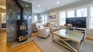 A living room with a stone fireplace, two armchairs, a TV, and a dining table. - Newly Constructed 3 Bedroom, 2 Bath Home on 12.5 Acres, Water Access and Views (WestBrook)