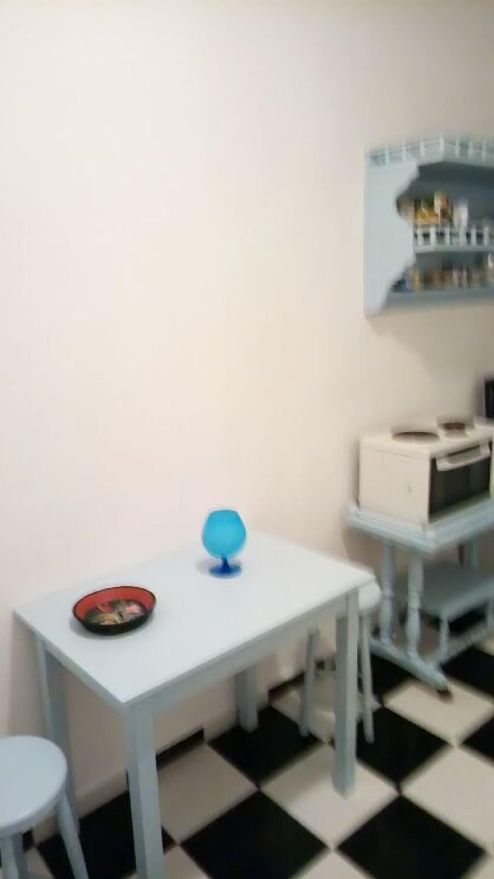 Ein kleiner Raum mit einem weißen Tisch, einem blauen Globus und einer roten Schüssel darauf. Der Boden ist schwarz-weiß kariert.