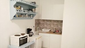 Een compacte keuken met een magnetron op een tafeltje, een koffiezetapparaat en een betegelde achterwand.