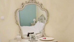 Een kamer met een wit aanrecht, een spiegel en een bed.