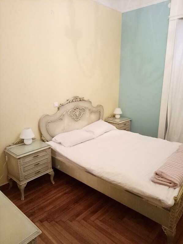 A single bed with a wooden headboard, two bedside tables with lamps, and a wooden floor.