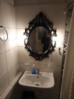 A bathroom with a white sink, a black ornate mirror, and a hand dryer.