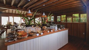 A buffet setup with various food items and utensils, wooden paneling, and hanging pendant lights. - Carambola Hotel (Porto Seguro)
