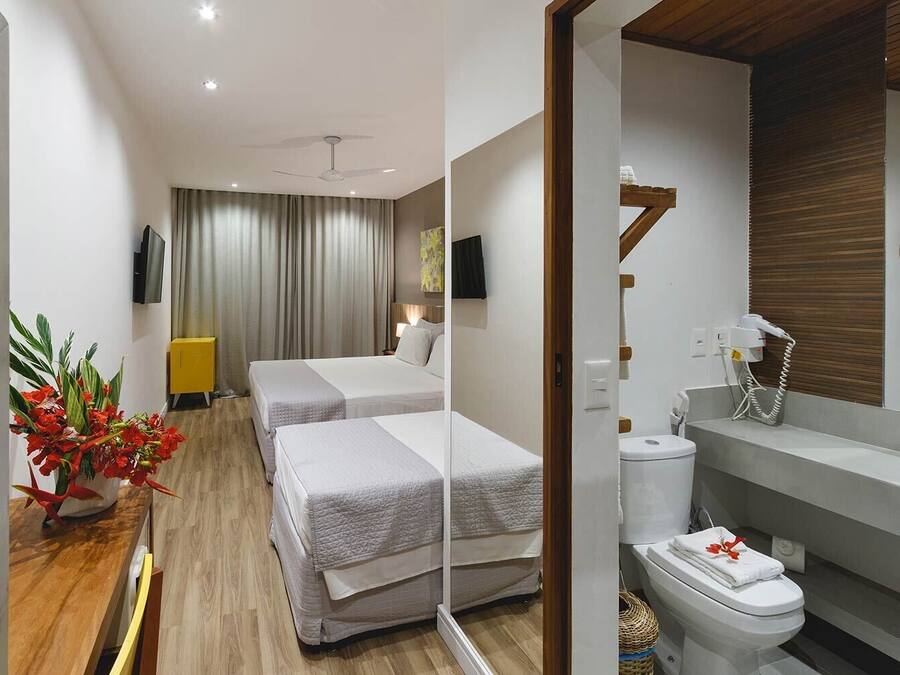 Une chambre d’hôtel avec deux lits, une télévision, un ventilateur de plafond, une salle de bain avec des toilettes et un lavabo, et un plancher en bois.