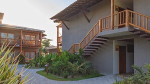 A hotel with a wooden staircase leading to a balcony, surrounded by lush greenery and a paved walkway. - Carambola Hotel (Porto Seguro)