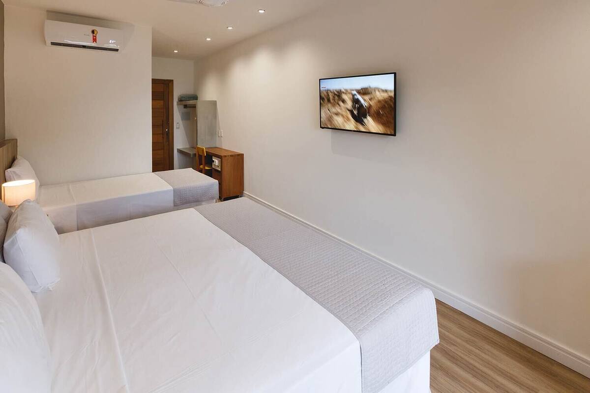 Une chambre d’hôtel avec deux lits, un téléviseur à écran plat fixé au mur, une table de chevet en bois et un petit bureau avec une chaise.