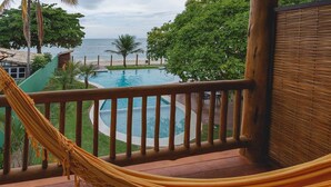 A wooden deck with a hammock, overlooking a pool and beach. - Carambola Hotel (Porto Seguro)