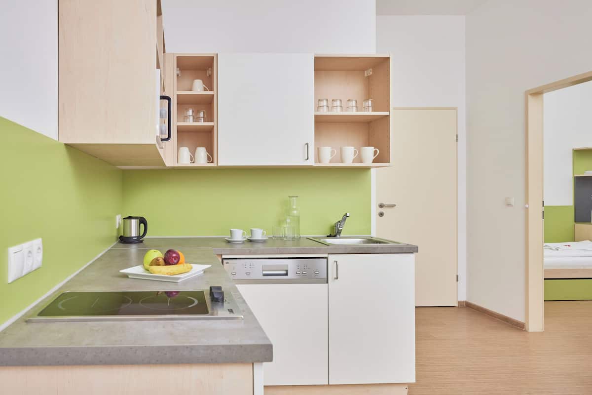 Una cocina compacta con lavavajillas, un fregadero y una encimera con frutas y un hervidor.