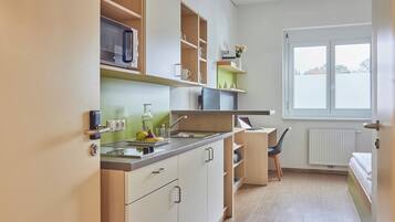 A compact kitchen with a microwave, sink, and shelves. There is a window with a view of trees.