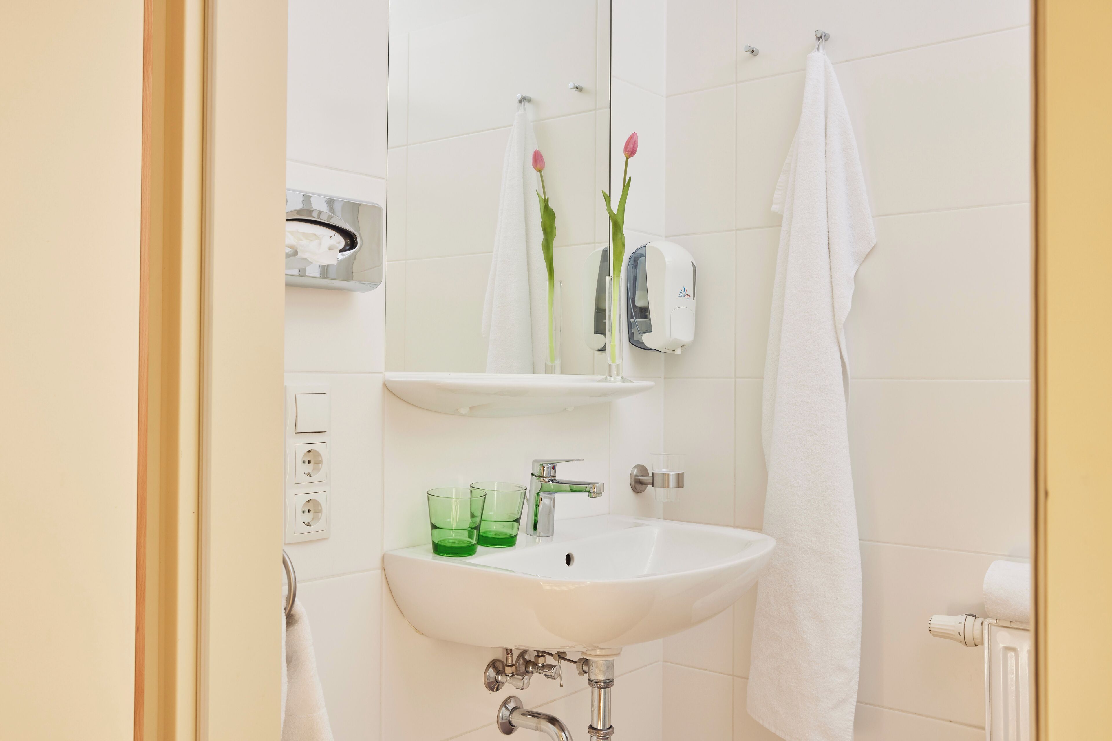 A bathroom with a white sink, green glasses, a towel rack, and a mirror.