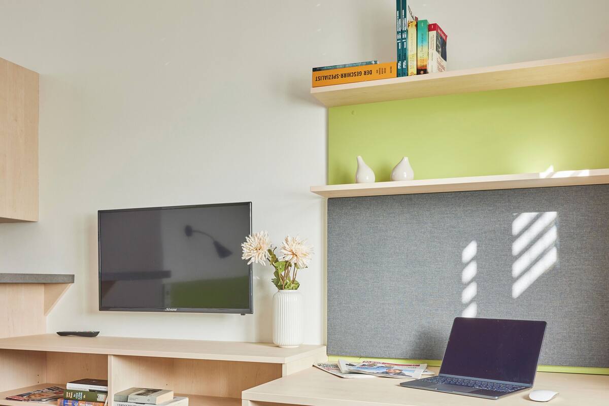 Espacio de oficina moderno con escritorio, silla, televisor, estanterías con libros y una pared divisoria.