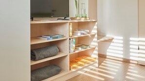 A modern room with a flat-screen TV on a wooden shelf, books, a mirror, and a window casting shadows on the floor. - I AM Hotel Leoben (Leoben)