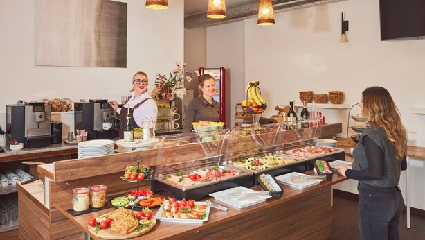 A buffet area with various food options, a refrigerator, and a coffee station. - I AM Hotel Leoben (Leoben)