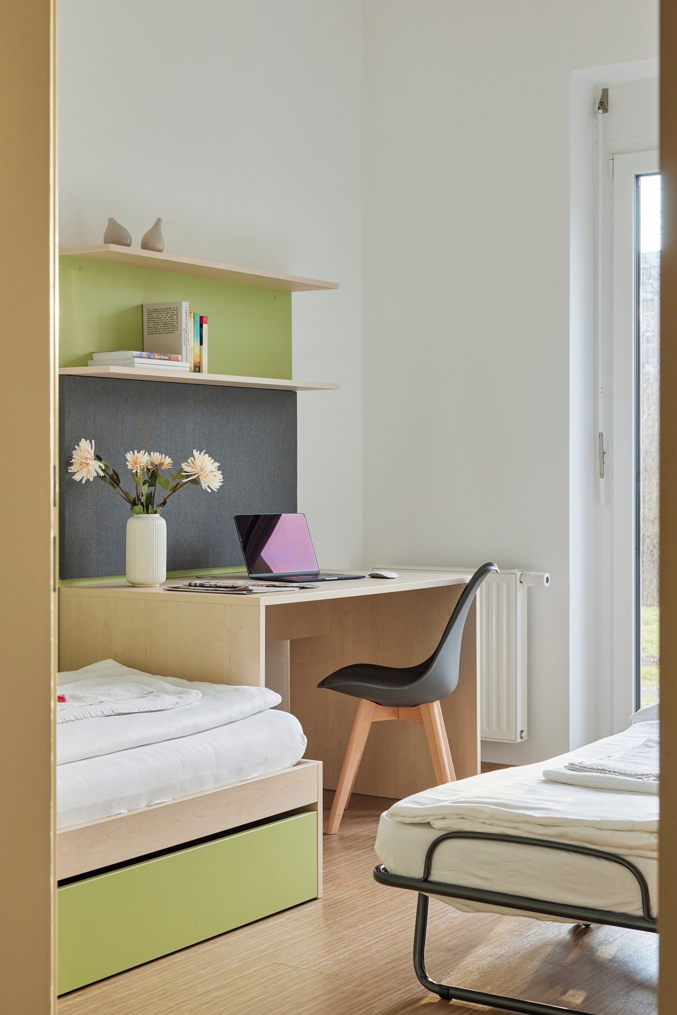 A bedroom with a bed, a desk with a laptop, a chair, and a radiator.