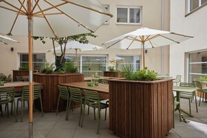 Un patio al aire libre con mesas y sillas de madera, rodeado de macetas y sombrillas.