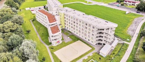 A multi-story hotel with a central courtyard, surrounded by greenery and a sports field.