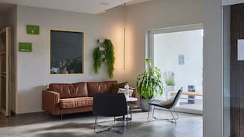 A modern hotel lobby with a brown leather sofa, a black chair, and a potted plant.