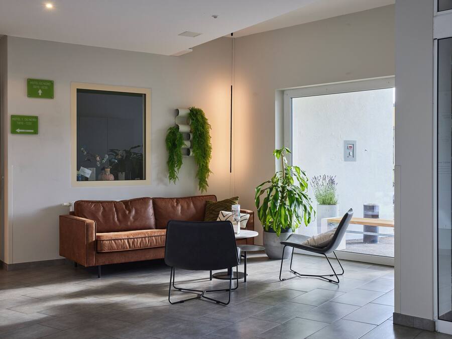Een moderne hotellobby met een bruine leren bank, een zwarte stoel en een potplant.