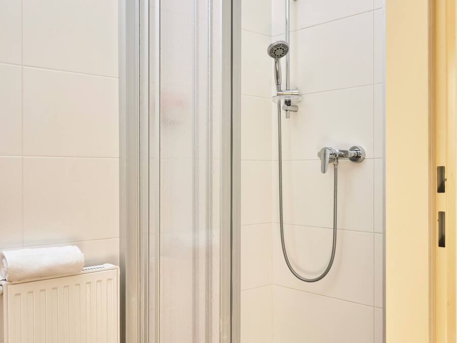 A glass-enclosed shower with a handheld showerhead and a wall-mounted faucet.