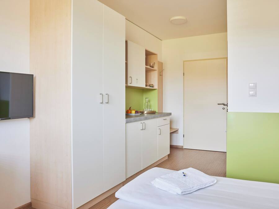 Una habitación de hotel con cama, televisión, kitchenette y puerta.