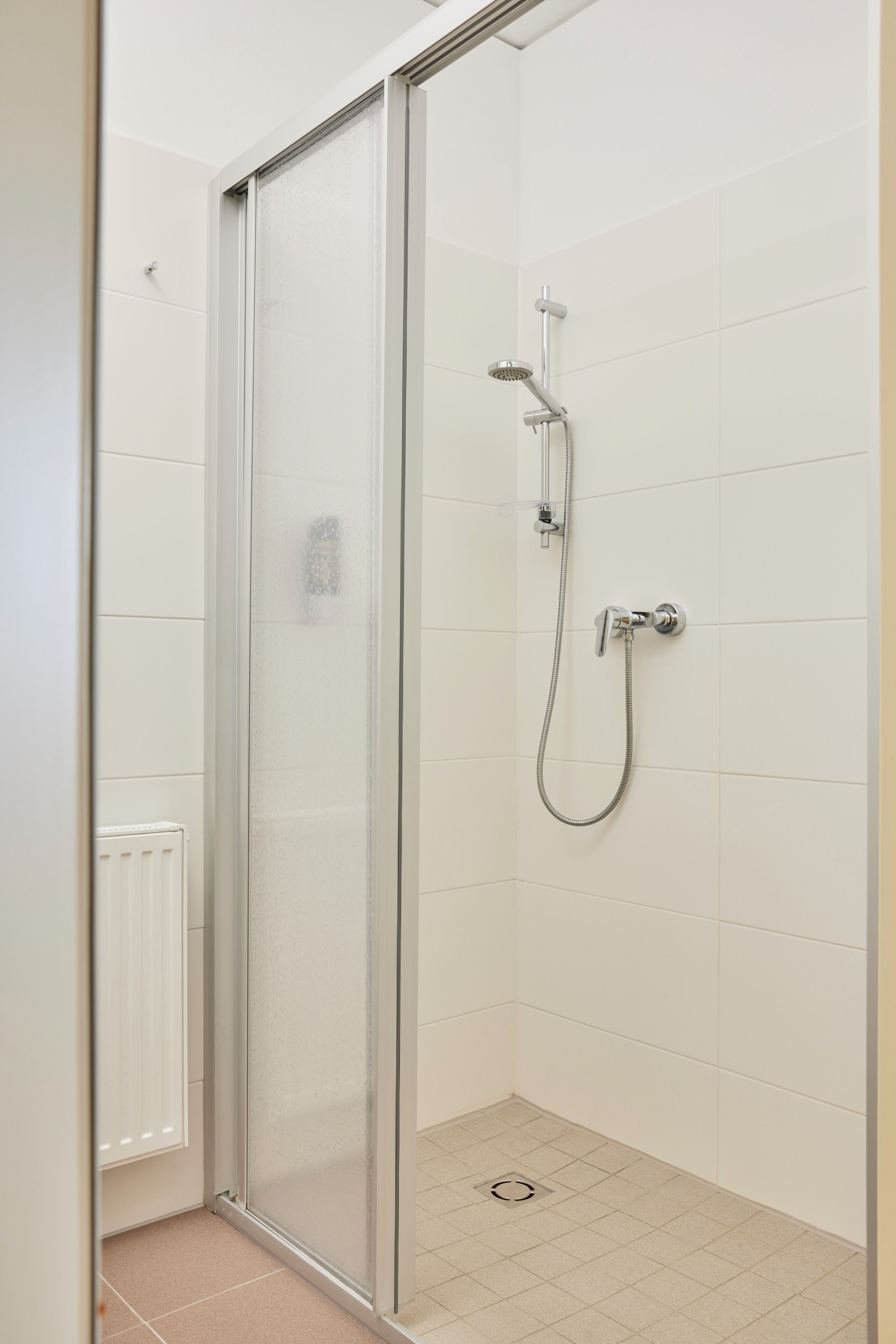 Ducha con mampara de vidrio, cabezal de ducha de mano y grifo empotrado.