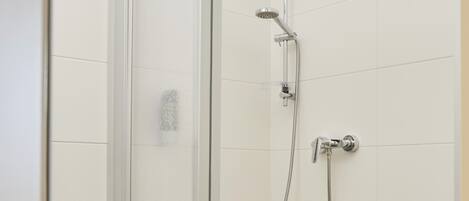 Ducha con mampara de vidrio, cabezal de ducha de mano y grifo empotrado.