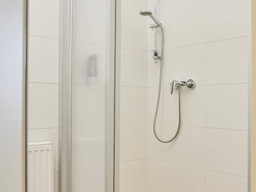 Ducha con mampara de vidrio, cabezal de ducha de mano y grifo empotrado.