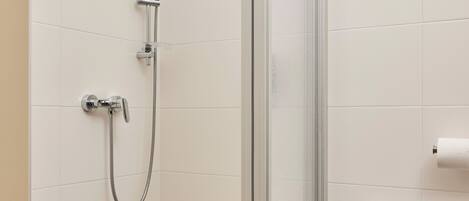 A shower with a glass door, a towel dispenser, and a radiator in a tiled bathroom.