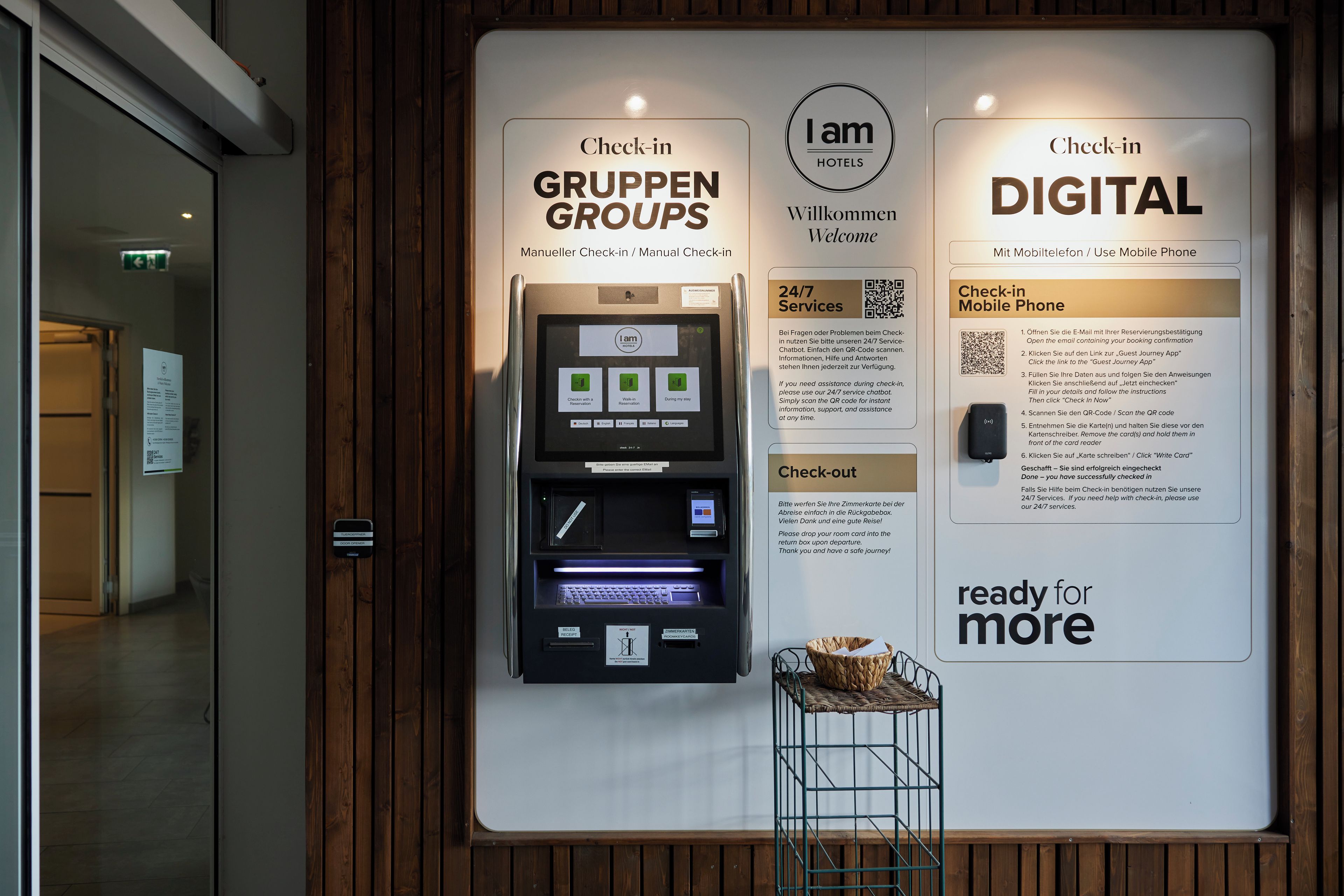 Un kiosque numérique pour l’enregistrement, avec des instructions pour l’arrivée et le départ, un code QR pour l’enregistrement sur mobile, et un panneau indiquant que les services sont disponibles 24 heures sur 24, 7 jours sur 7.