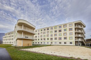 A multi-story hotel with balconies, a sandy courtyard, and a mountainous backdrop. - I AM HOTELS Leoben (Leoben)