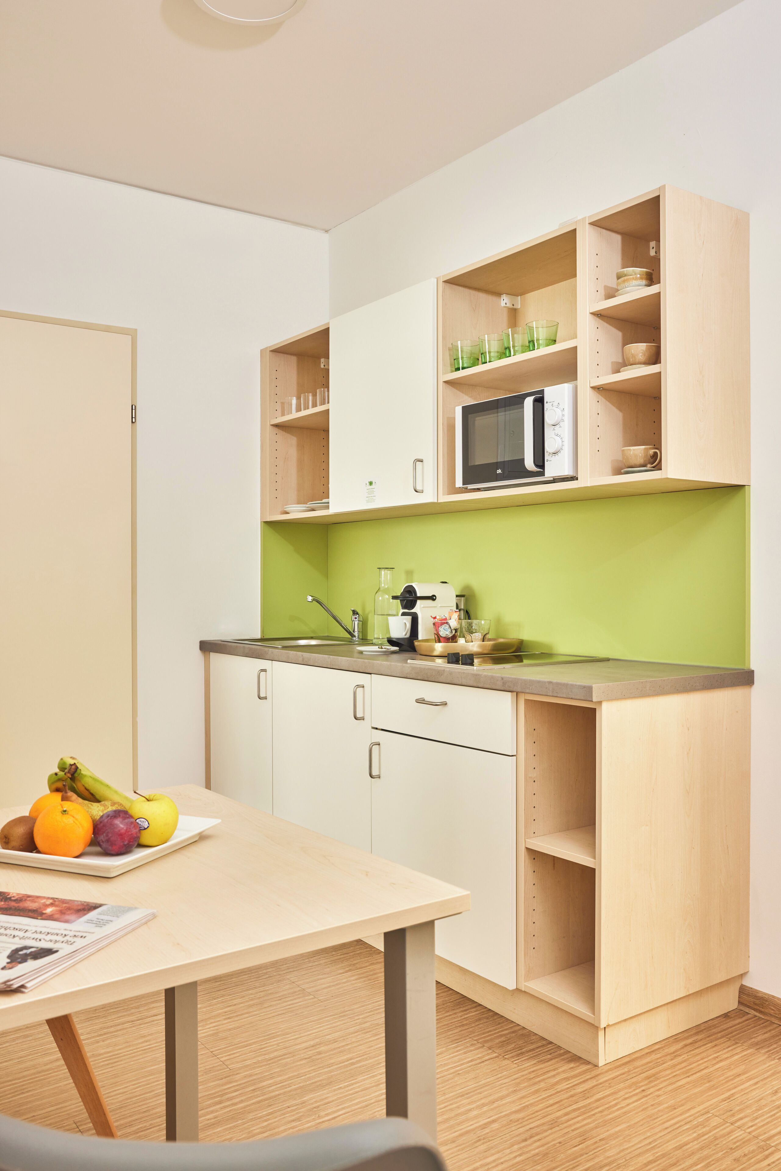 A compact kitchen with a microwave, a sink, and a green backsplash.