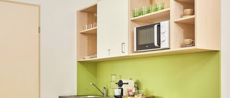 A compact kitchen with a microwave, a sink, and a green backsplash.